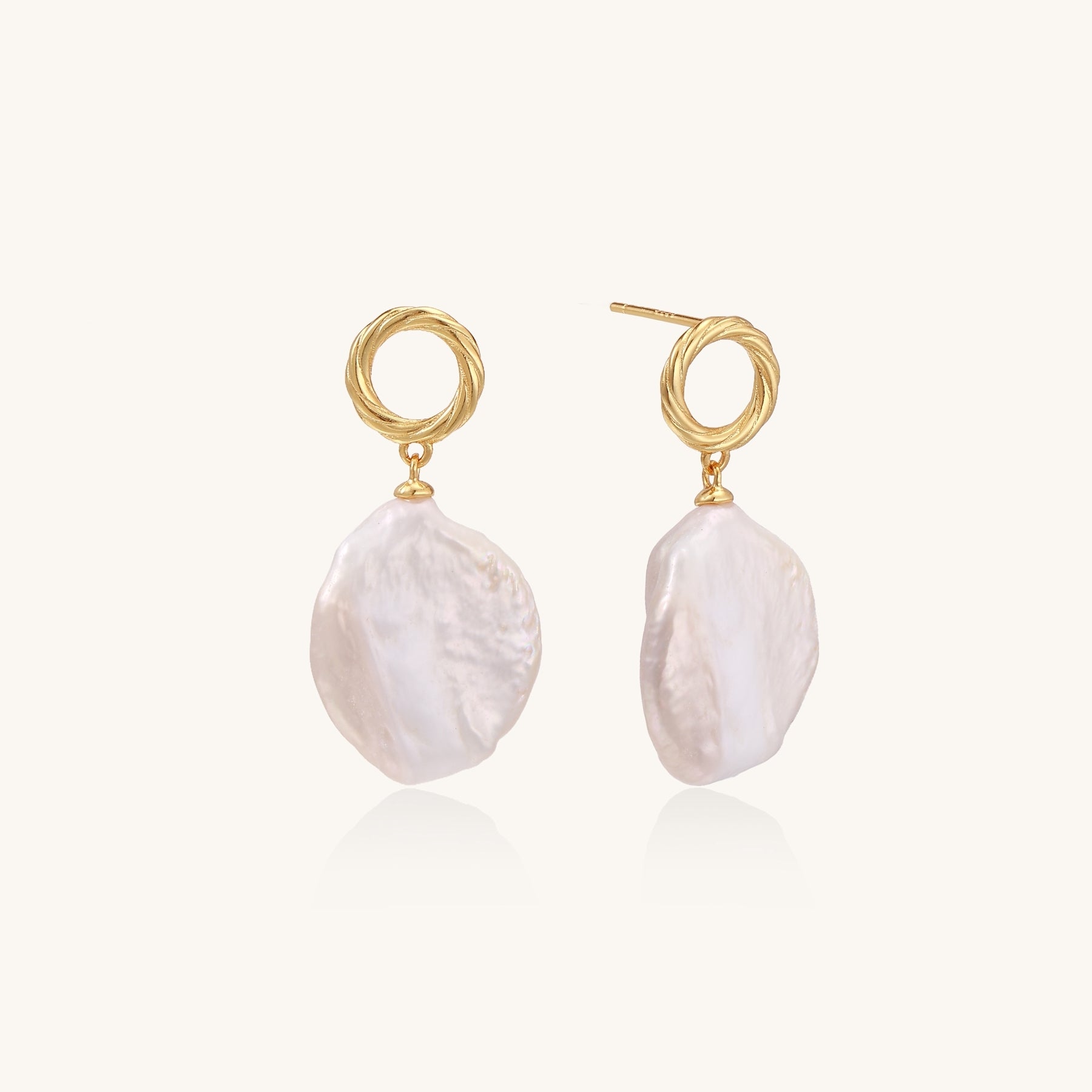 Gold-plated twisted stud earrings with large blush baroque pearls hanging elegantly on white background.