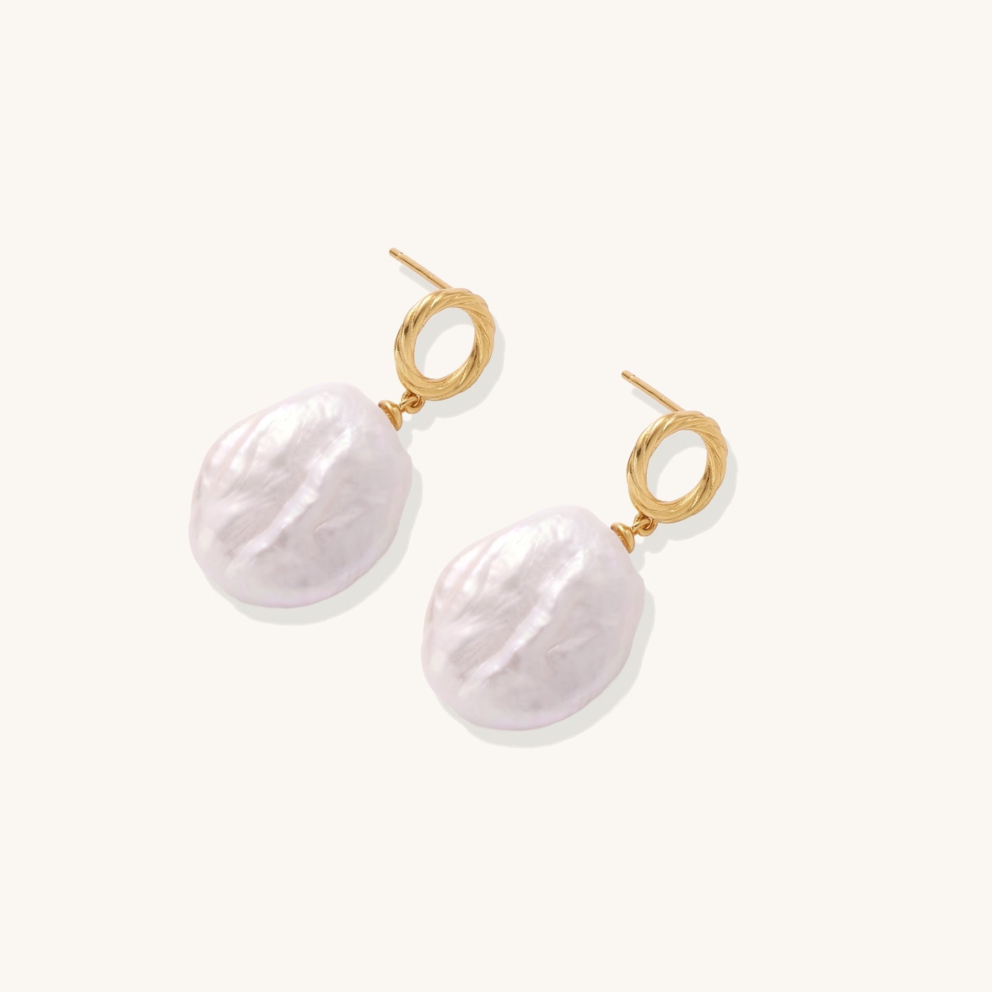 Gold-plated twisted stud earrings with large blush baroque pearls hanging elegantly on white background.