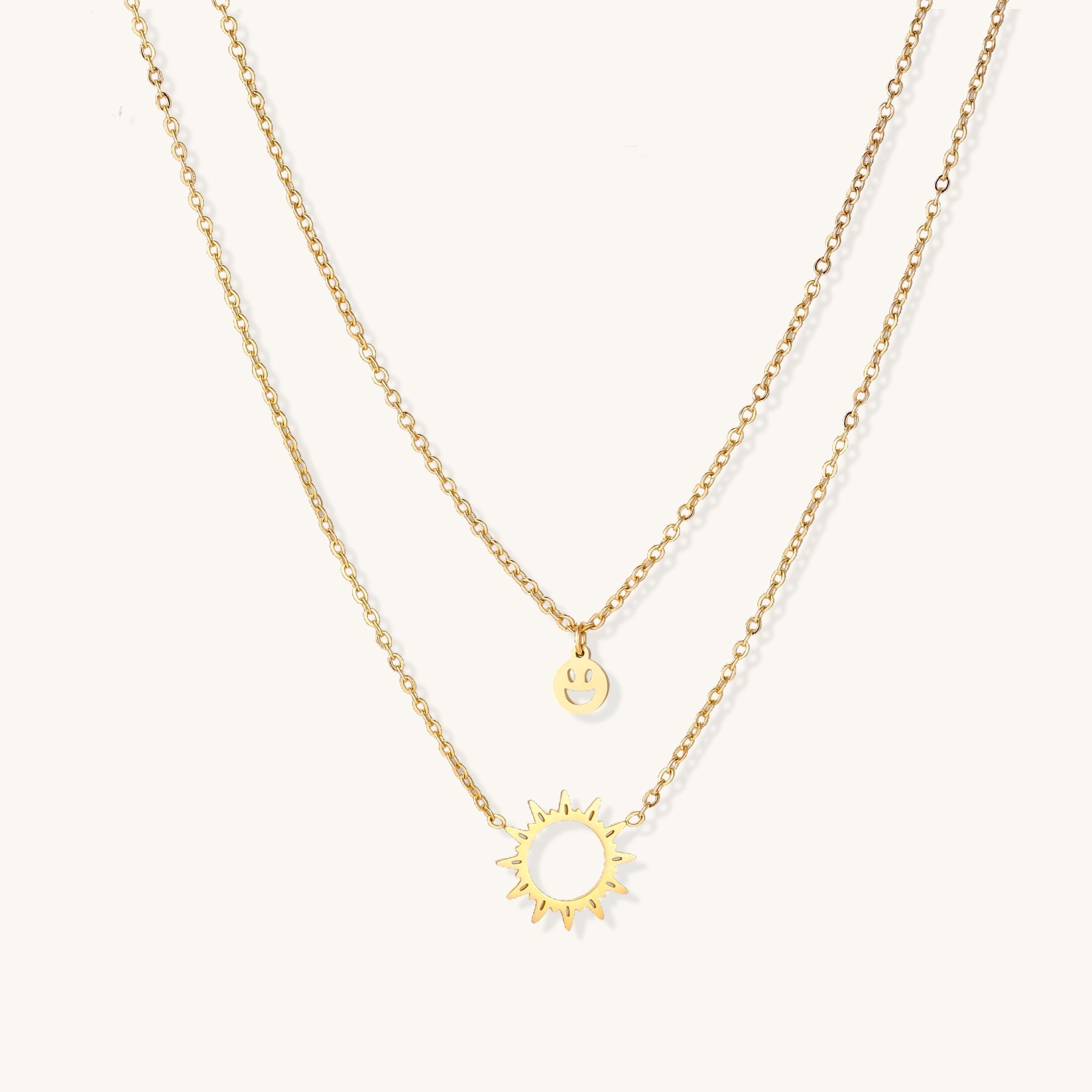 Delicate gold-plated layered necklace with smiley face and sun pendants on white background, showing adjustable chain.